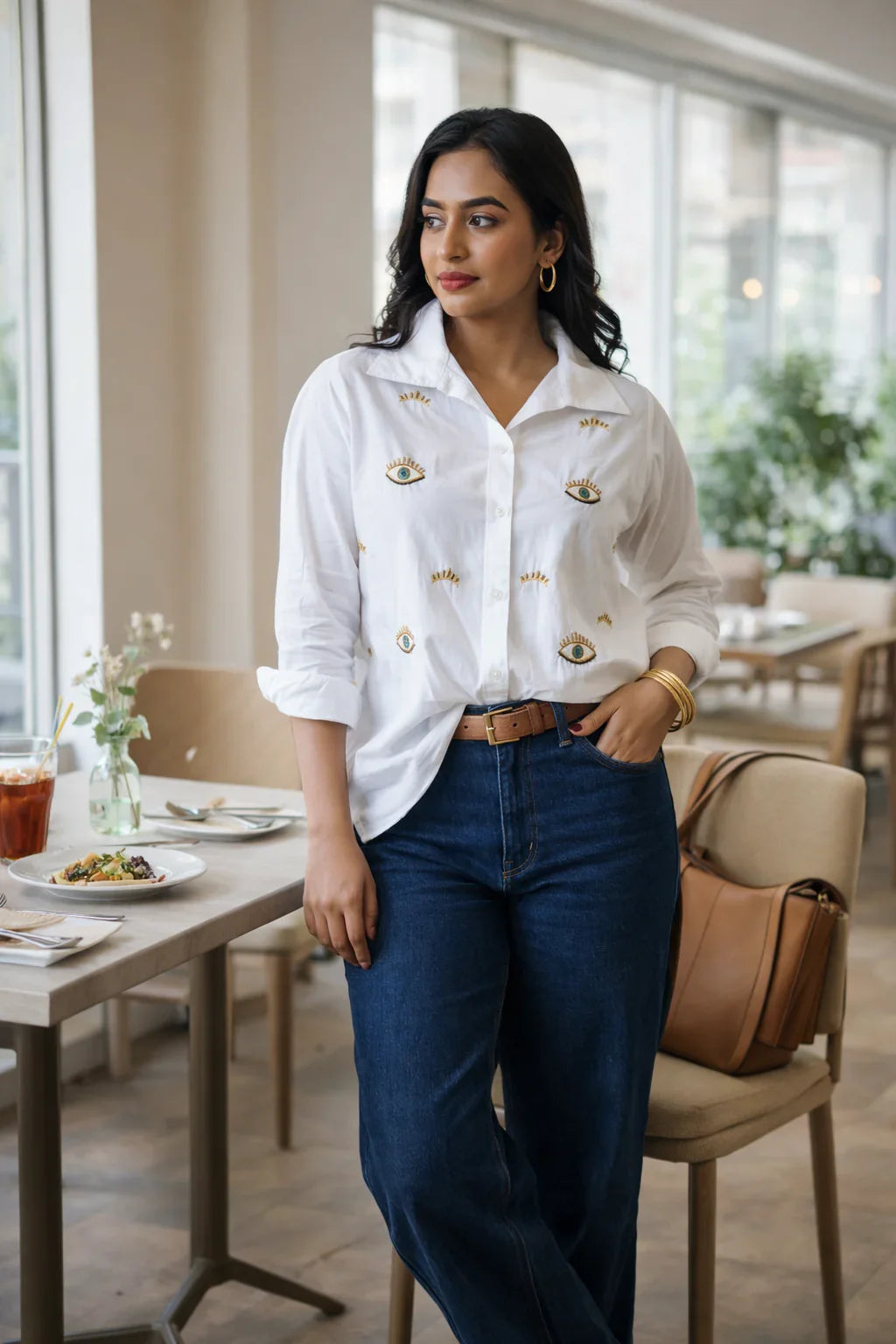 Woman in white embroidered shirt and blue jeans at a cafe