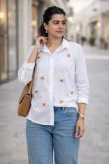 White button-down shirt with popcorn embroidery, paired with blue jeans and a tan bag for casual everyday style.
