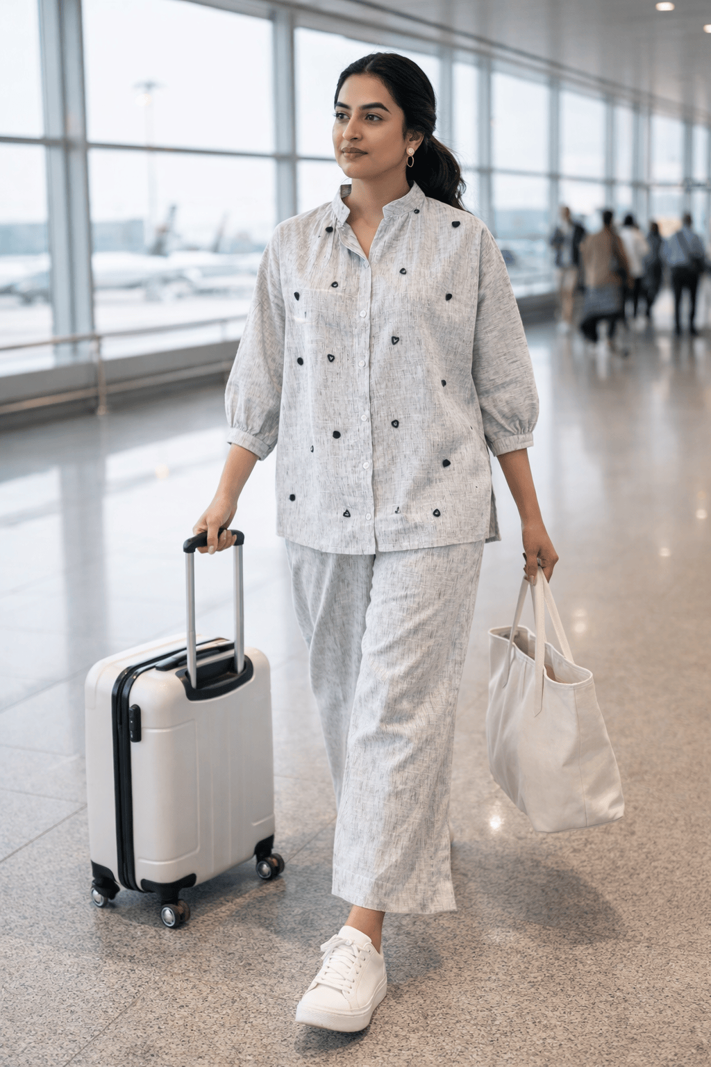 Woman in stylish gray co-ord set with black dot details, walking through airport with suitcase and tote bag