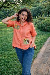 Orange embroidered shirt with floral patches, paired with blue jeans, worn in a lush green park.