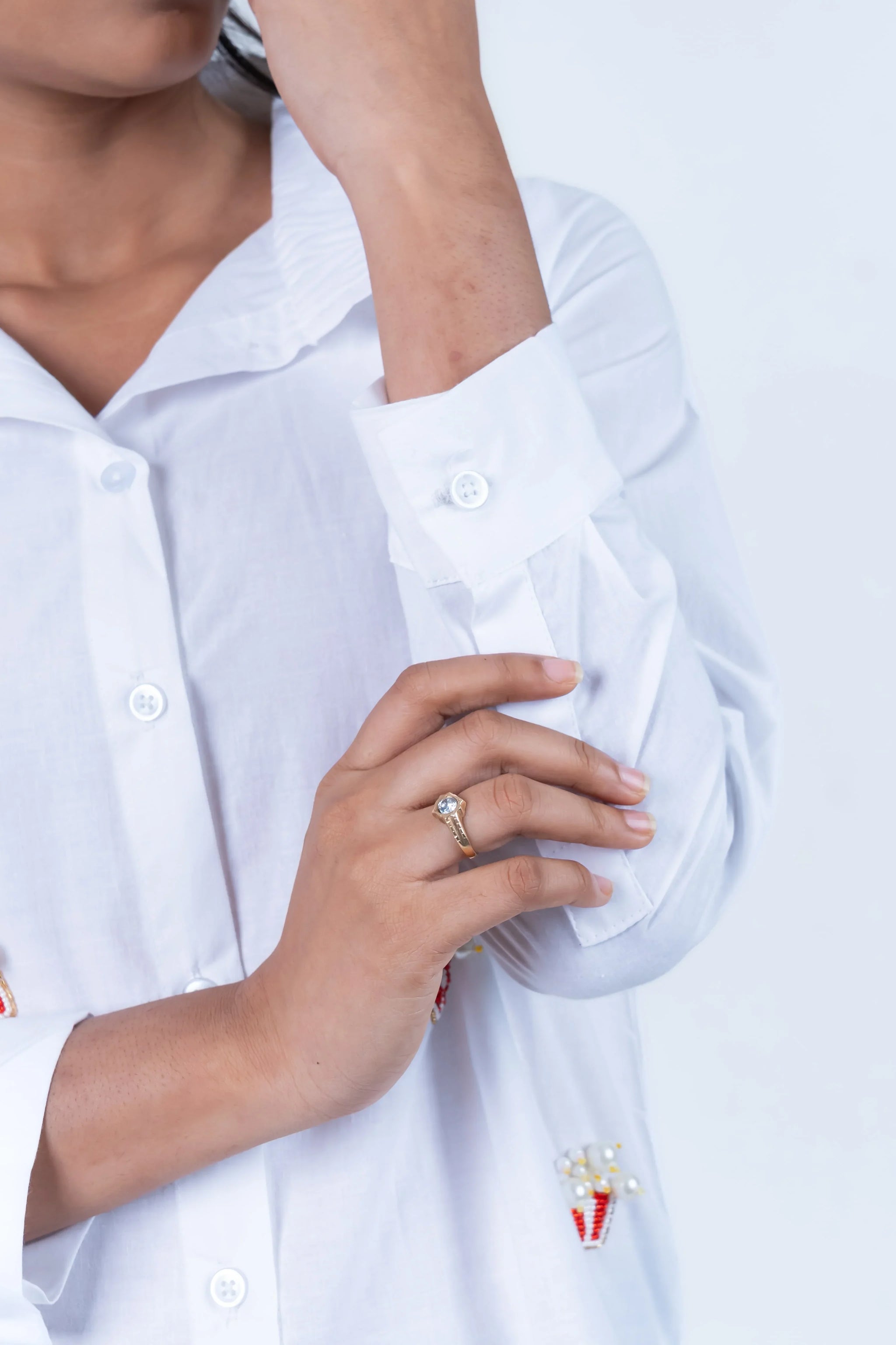 Woman in white shirt with gold ring and decorative brooch, showcasing elegant everyday style.