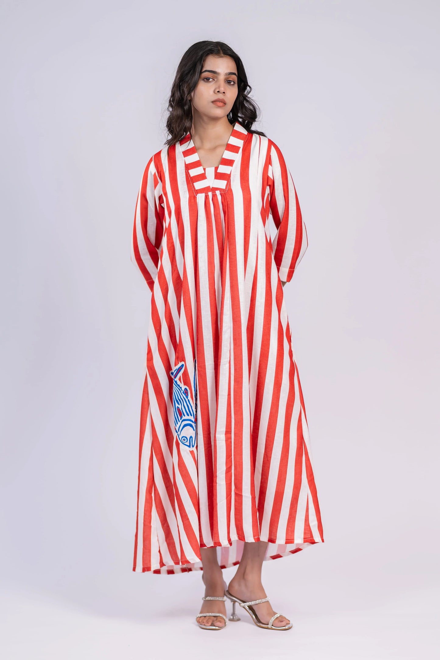 Woman wearing a red and white striped maxi dress with blue fish embroidery, standing indoors.