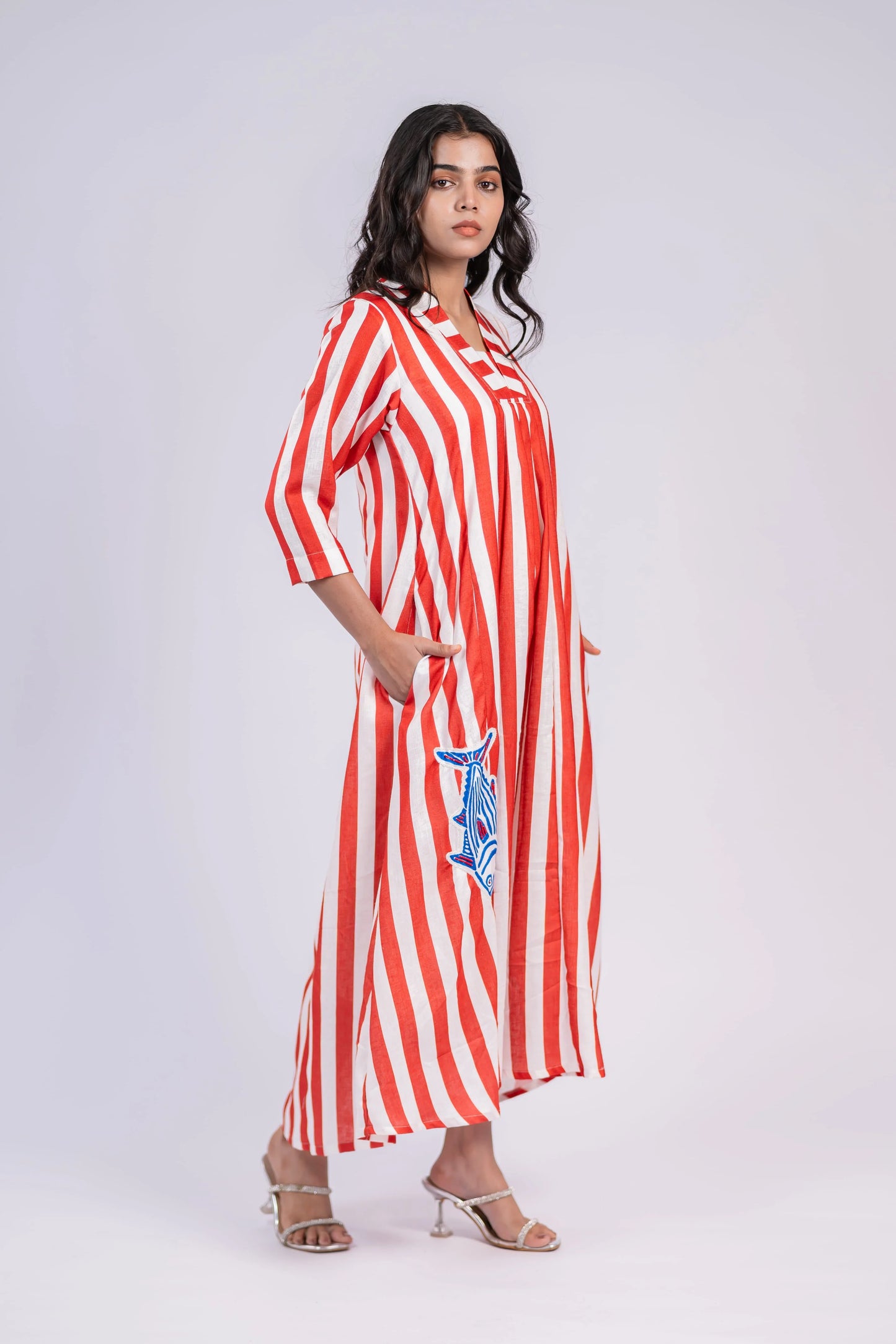 Woman wearing a red and white striped maxi dress with embroidered blue fish, three-quarter sleeves