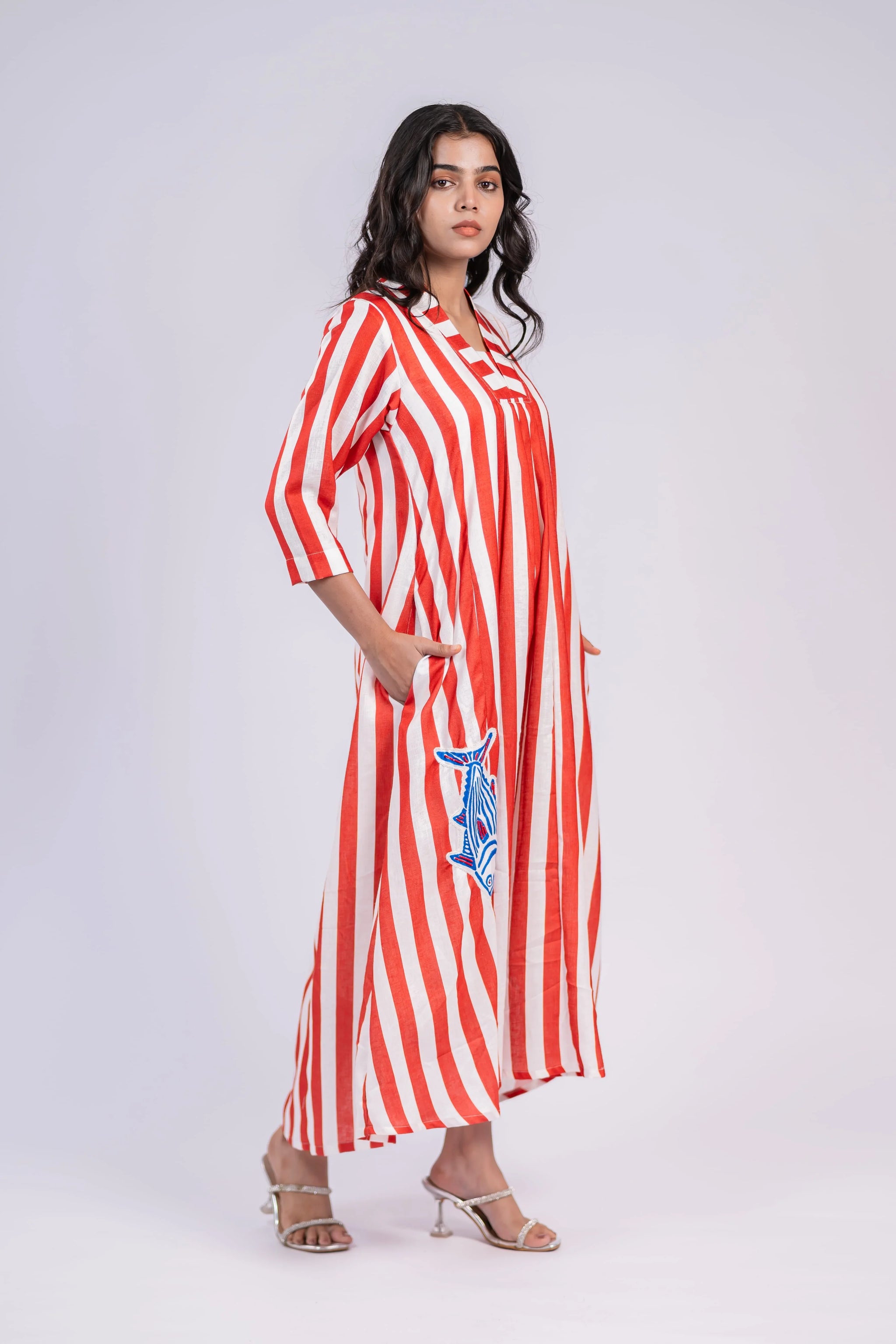 Woman wearing a red and white striped maxi dress with embroidered blue fish, three-quarter sleeves
