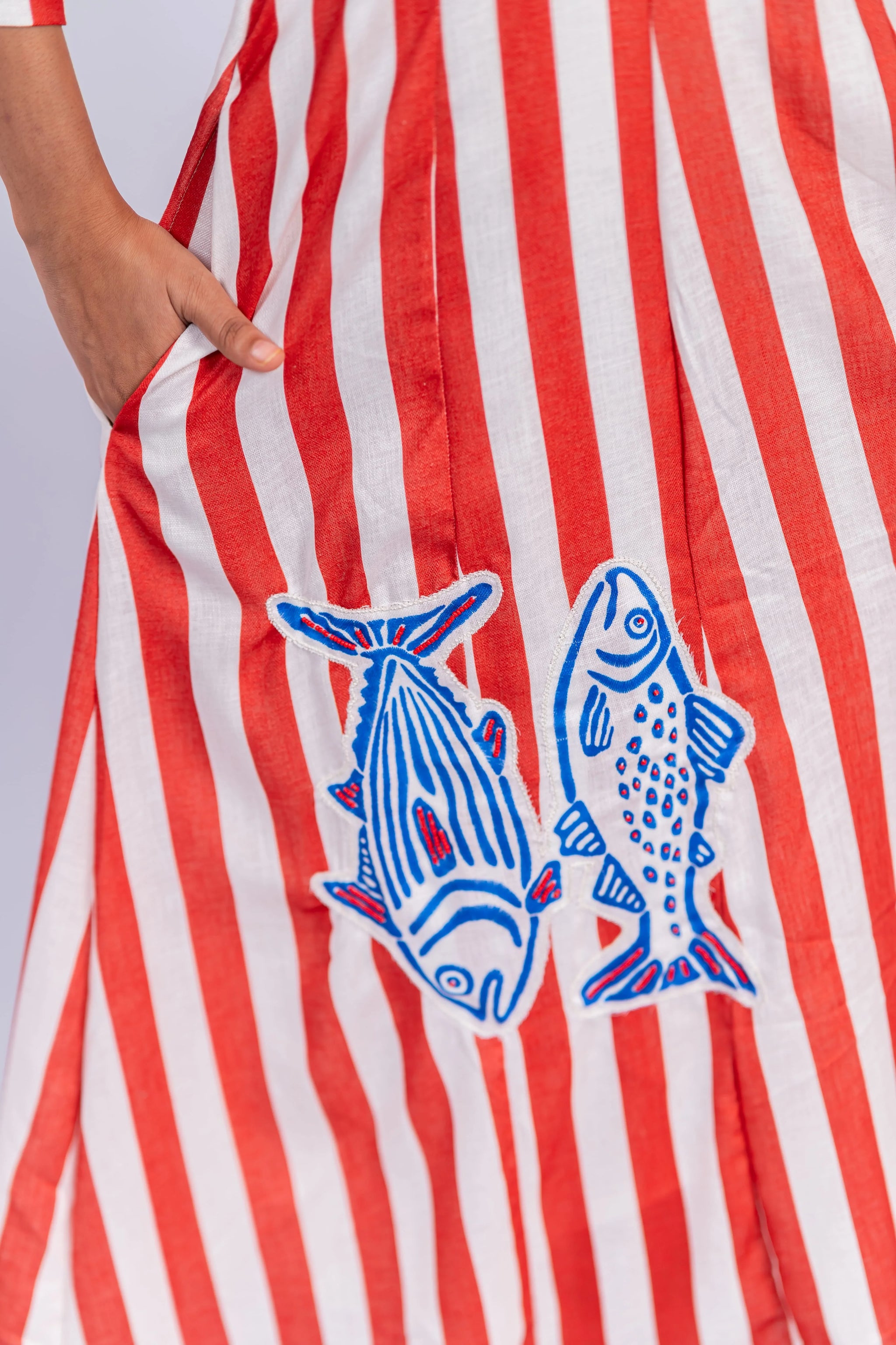 Red and white striped women's dress with blue fish embroidery and side pocket.