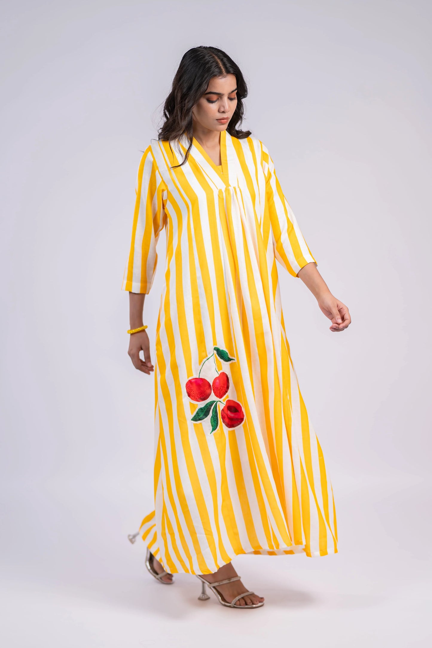 Woman wearing yellow and white striped maxi dress with cherry print, three-quarter sleeves