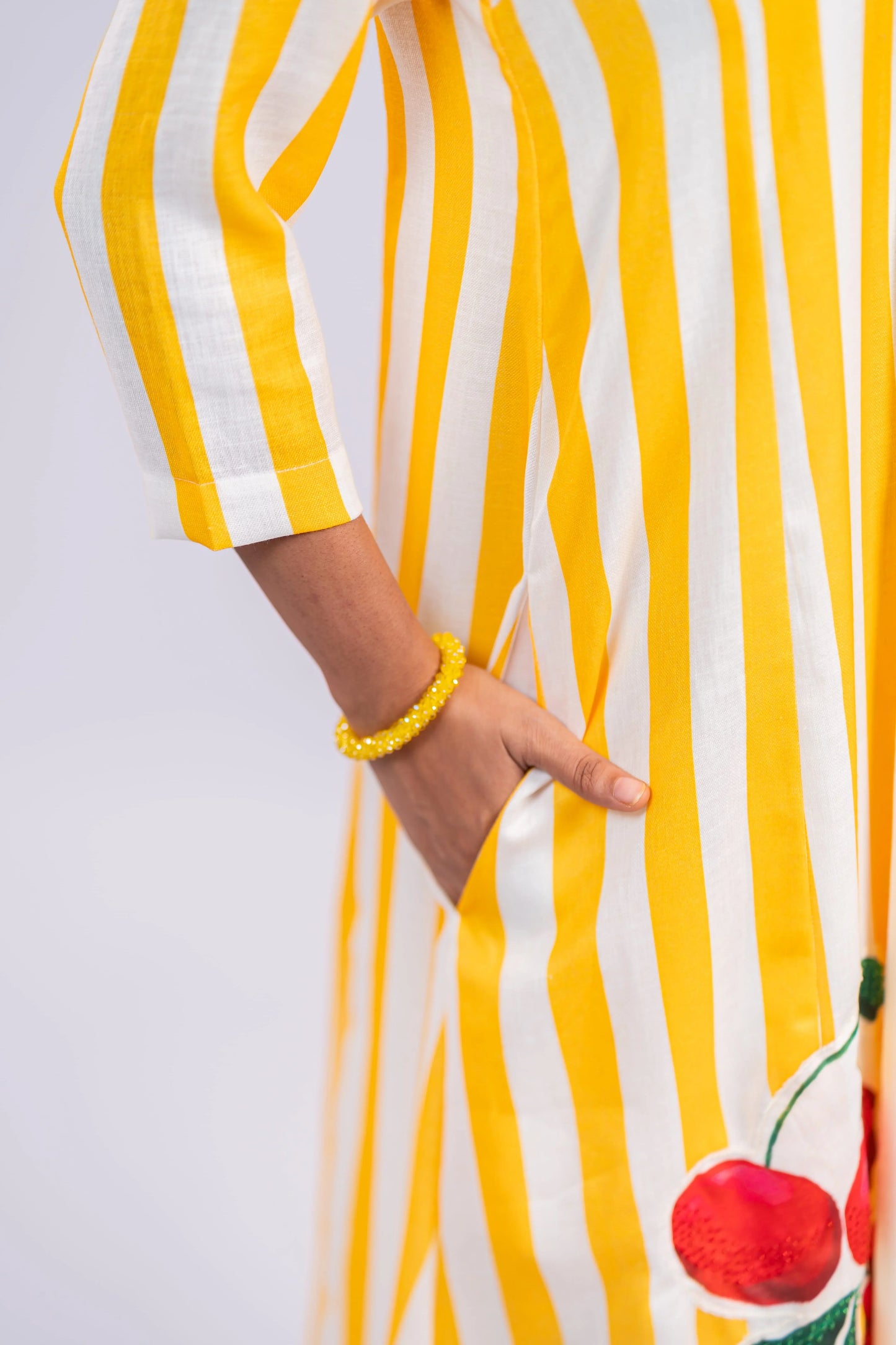 Woman wearing yellow and white striped dress with side pocket, cherry embroidery, yellow bracelet