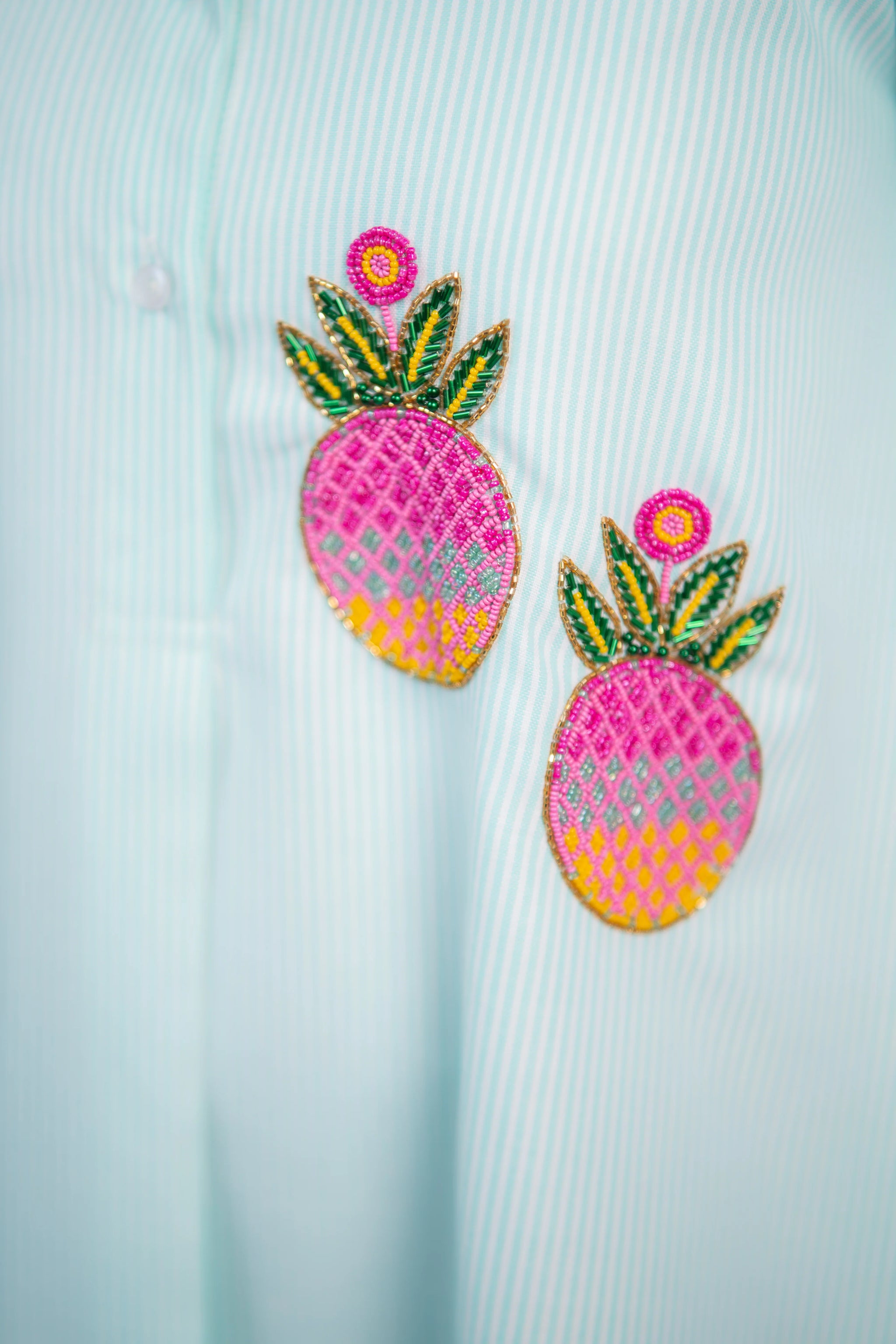 Beaded pineapple embroidery on striped women's shirt, vibrant pink and green design