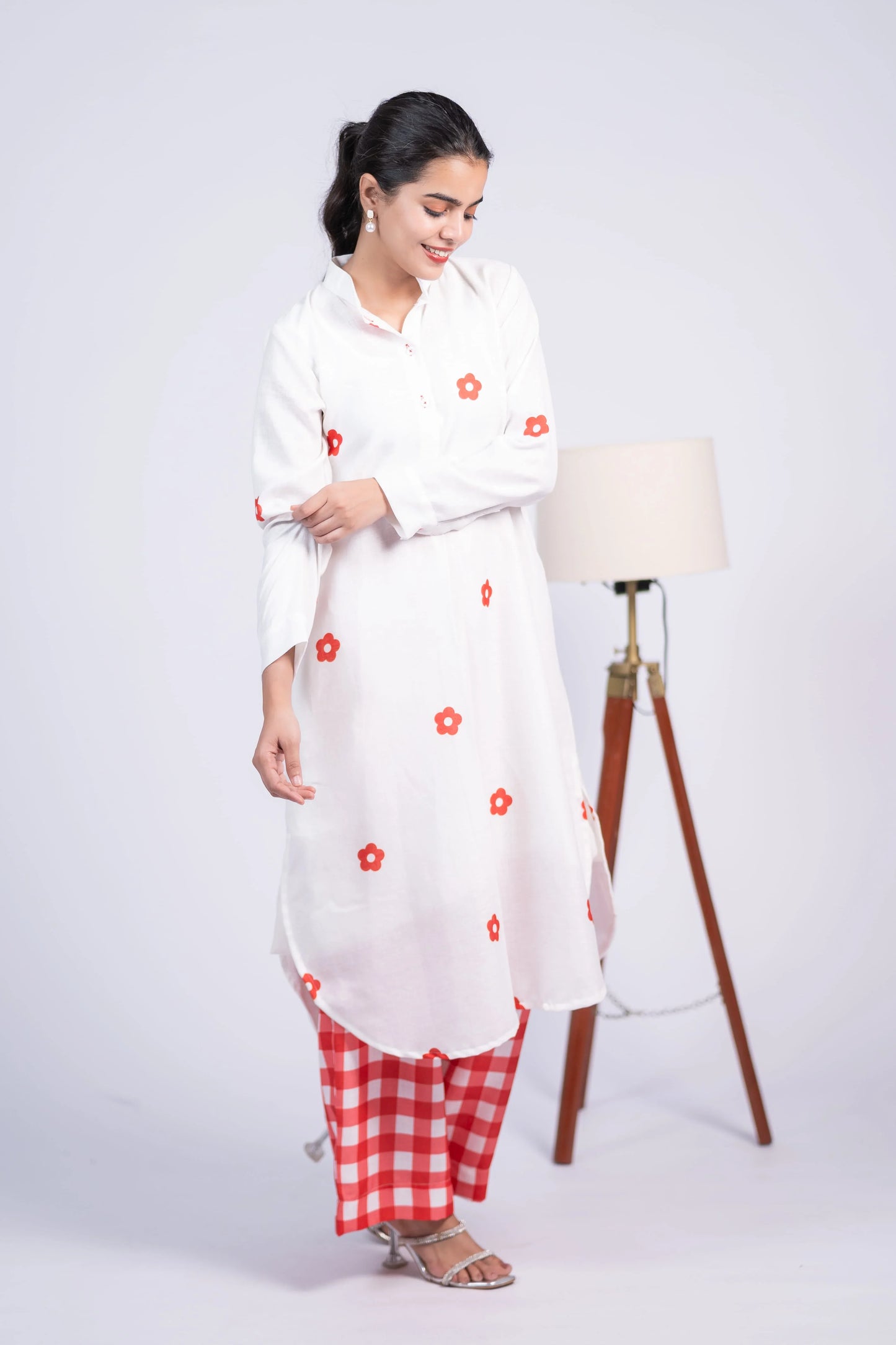 Woman in white floral kurta with red checkered pants and silver heels standing indoors