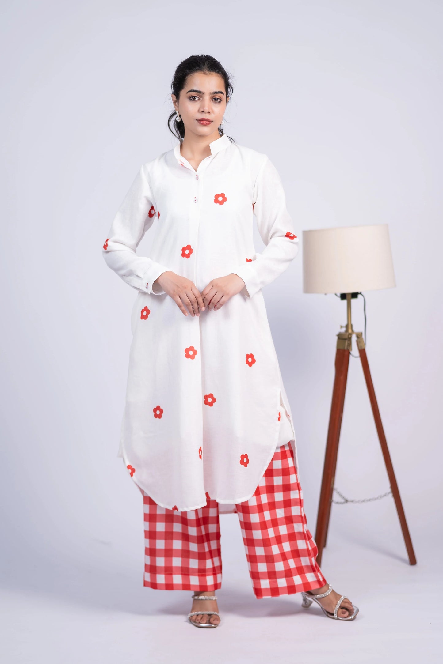 Woman wearing a white floral kurta and red checkered palazzo pants, standing indoors
