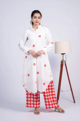 Woman wearing a white floral kurta and red checkered palazzo pants, standing indoors