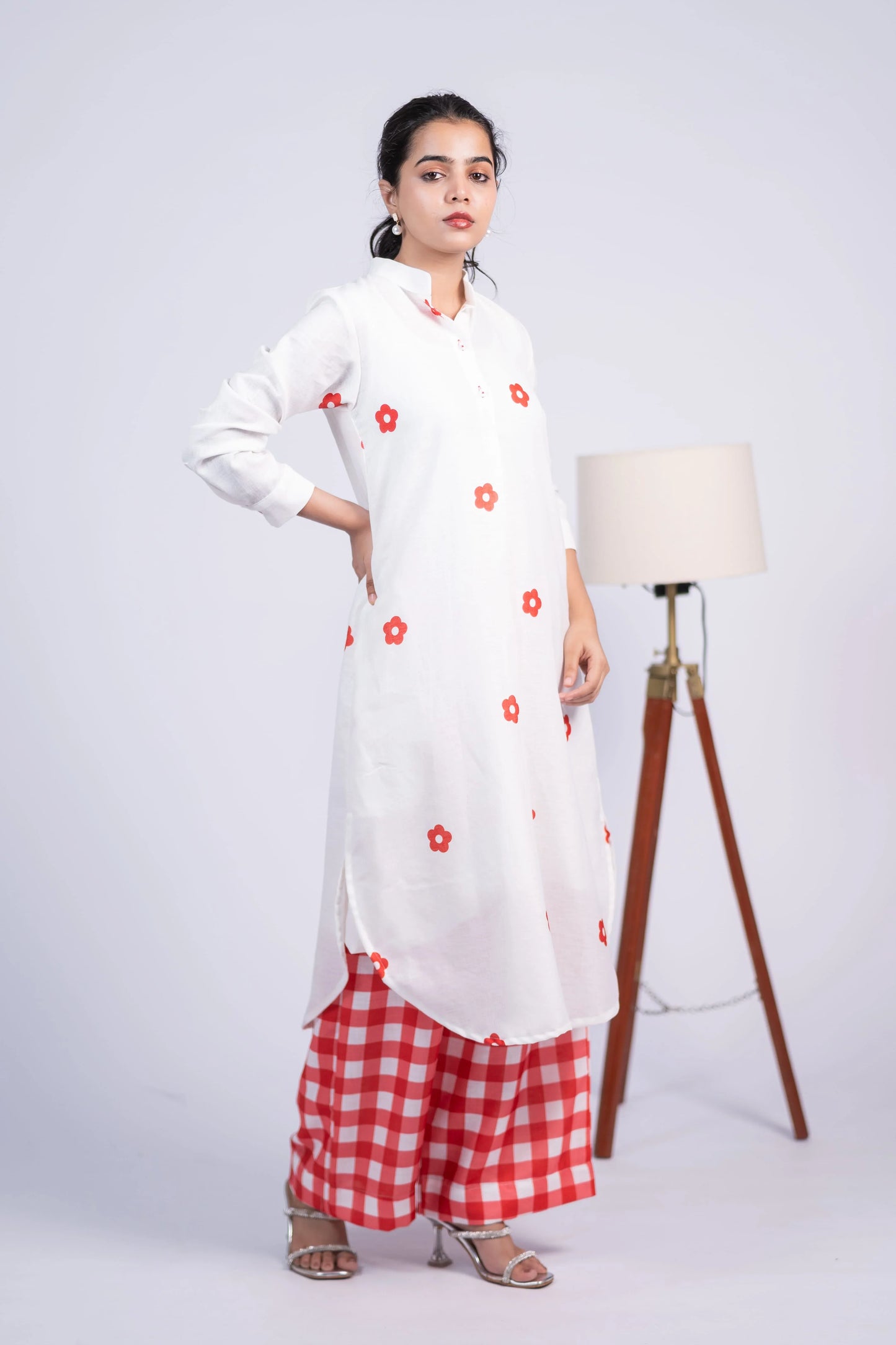 Woman in white floral kurta with red checkered palazzo pants, studio background