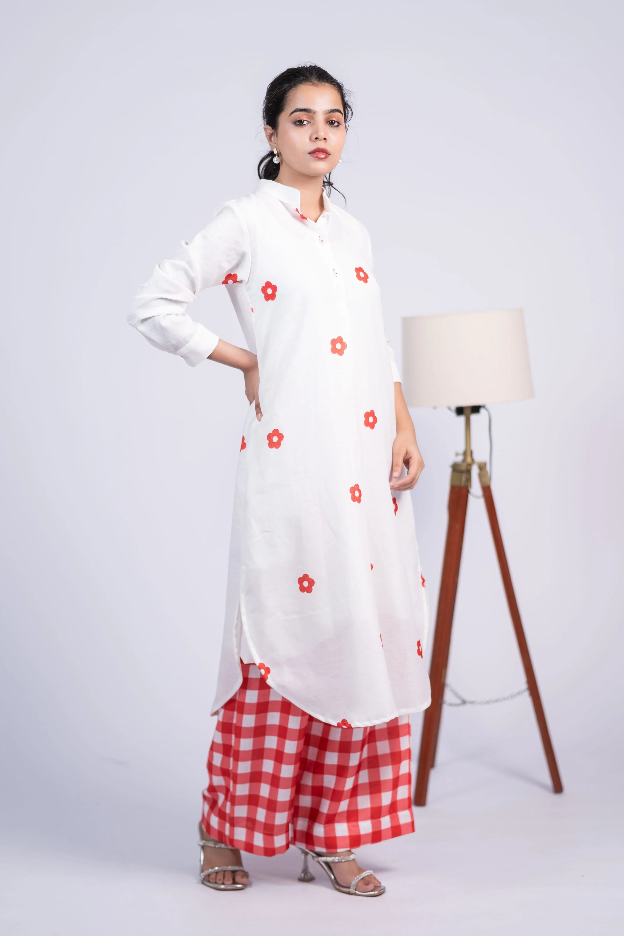 Woman in white floral kurta with red checkered palazzo pants, studio background