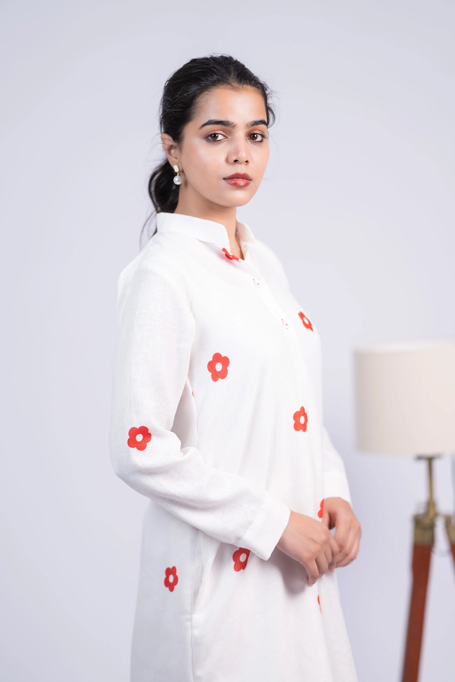 Woman in a white long-sleeve kurti with red floral prints, posing indoors