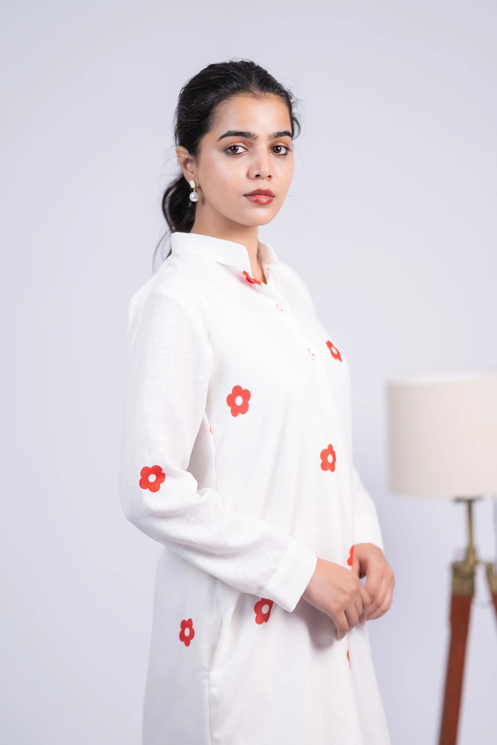 Woman in a white long-sleeve kurti with red floral prints, posing indoors