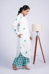 Woman in a white floral kurta and green checkered pants, standing near a floor lamp