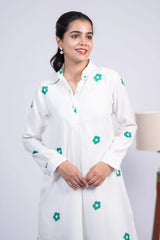 Woman wearing a white dress with green floral prints and long sleeves, posing indoors