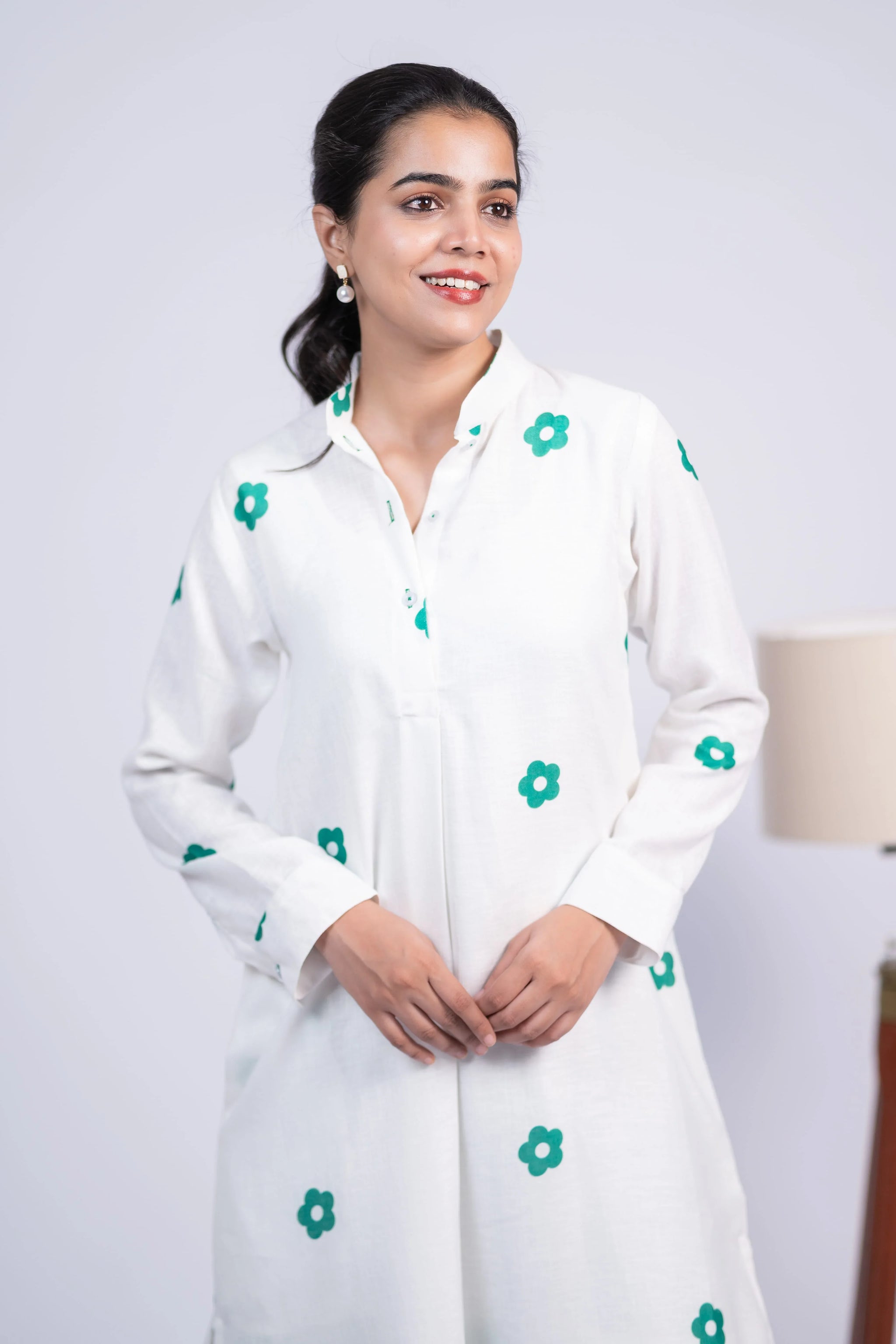 Woman wearing a white dress with green floral prints and long sleeves, posing indoors