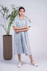 Woman in a light blue striped midi shirt dress with red accents, casual sneakers, indoor plant backdrop