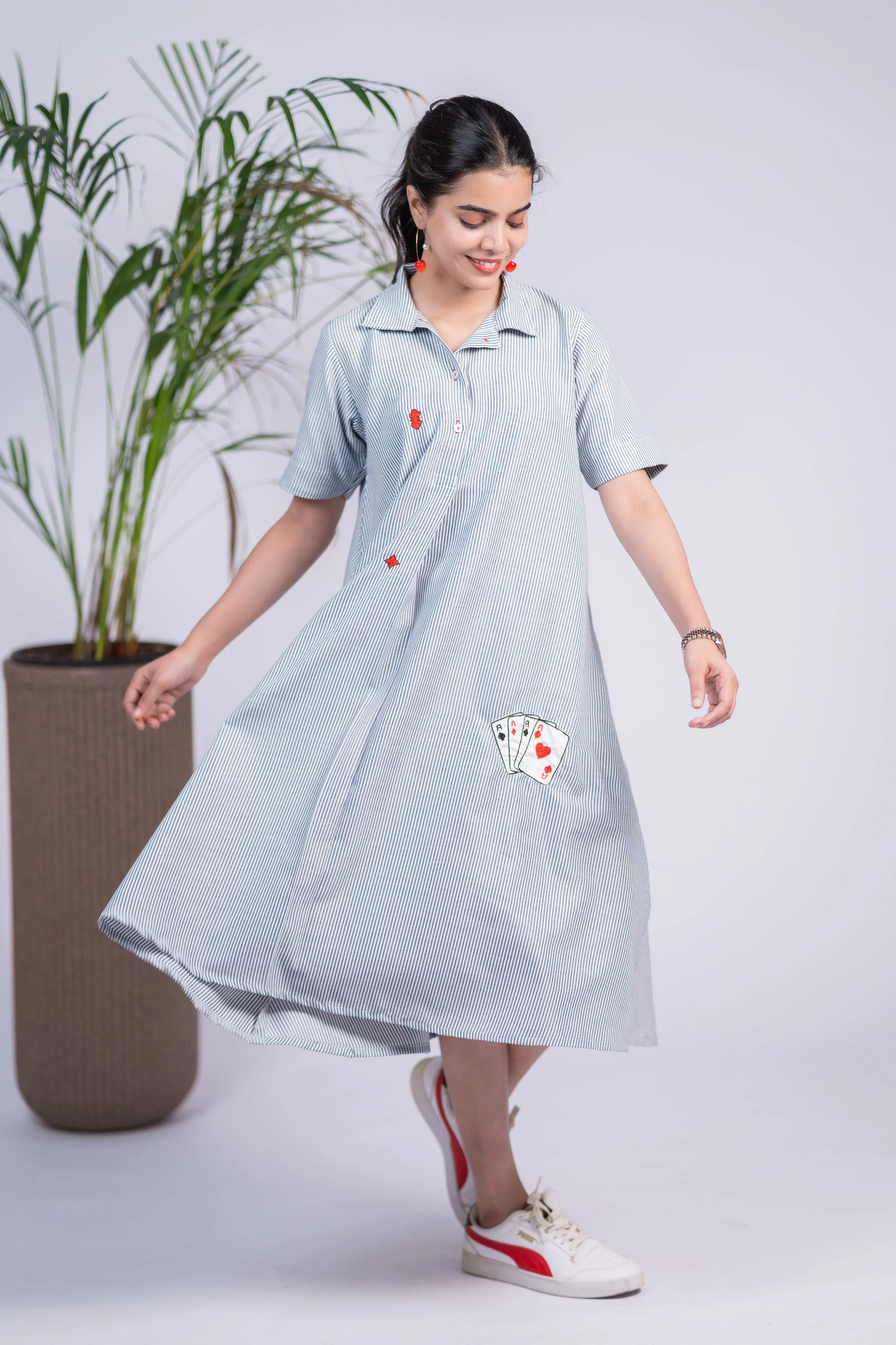 Woman wearing a striped midi dress with playing card motifs and casual sneakers, indoor setting