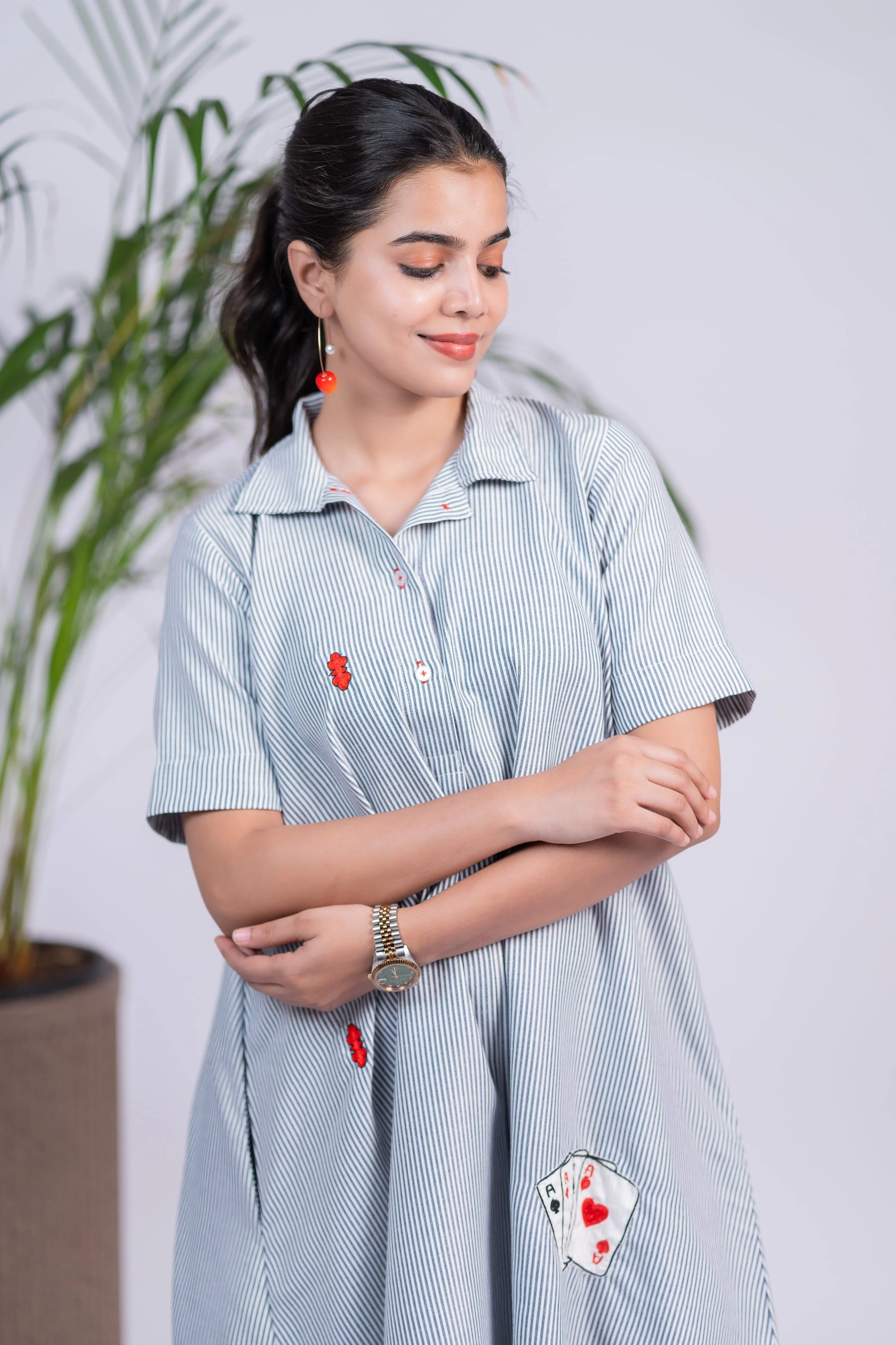 Woman in a blue striped dress with red cherry earrings, card patch embroidery, and casual style.