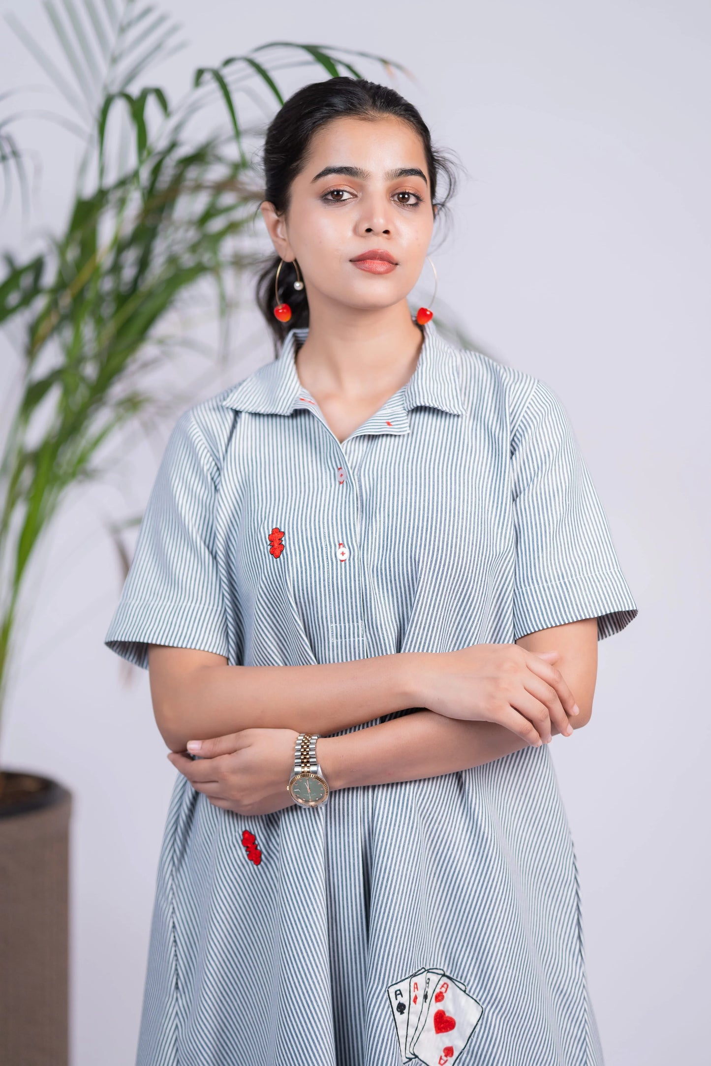 Woman in striped button-down dress with card patch and red earrings, indoor setting