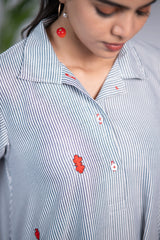 Close-up of a woman wearing a blue striped shirt with red floral embroidery and cherry earrings