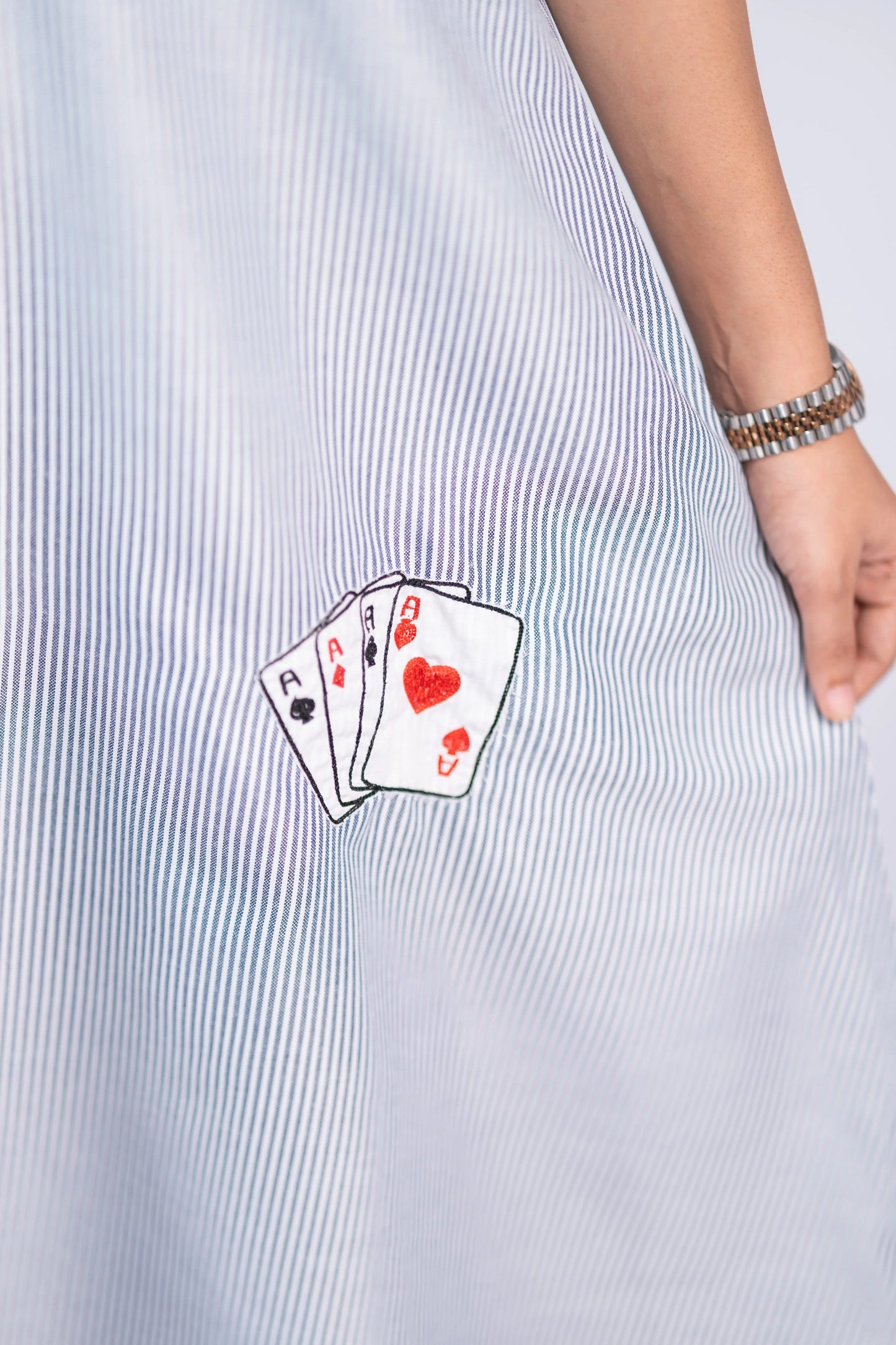 Close-up of a blue and white striped dress with embroidered playing cards detail