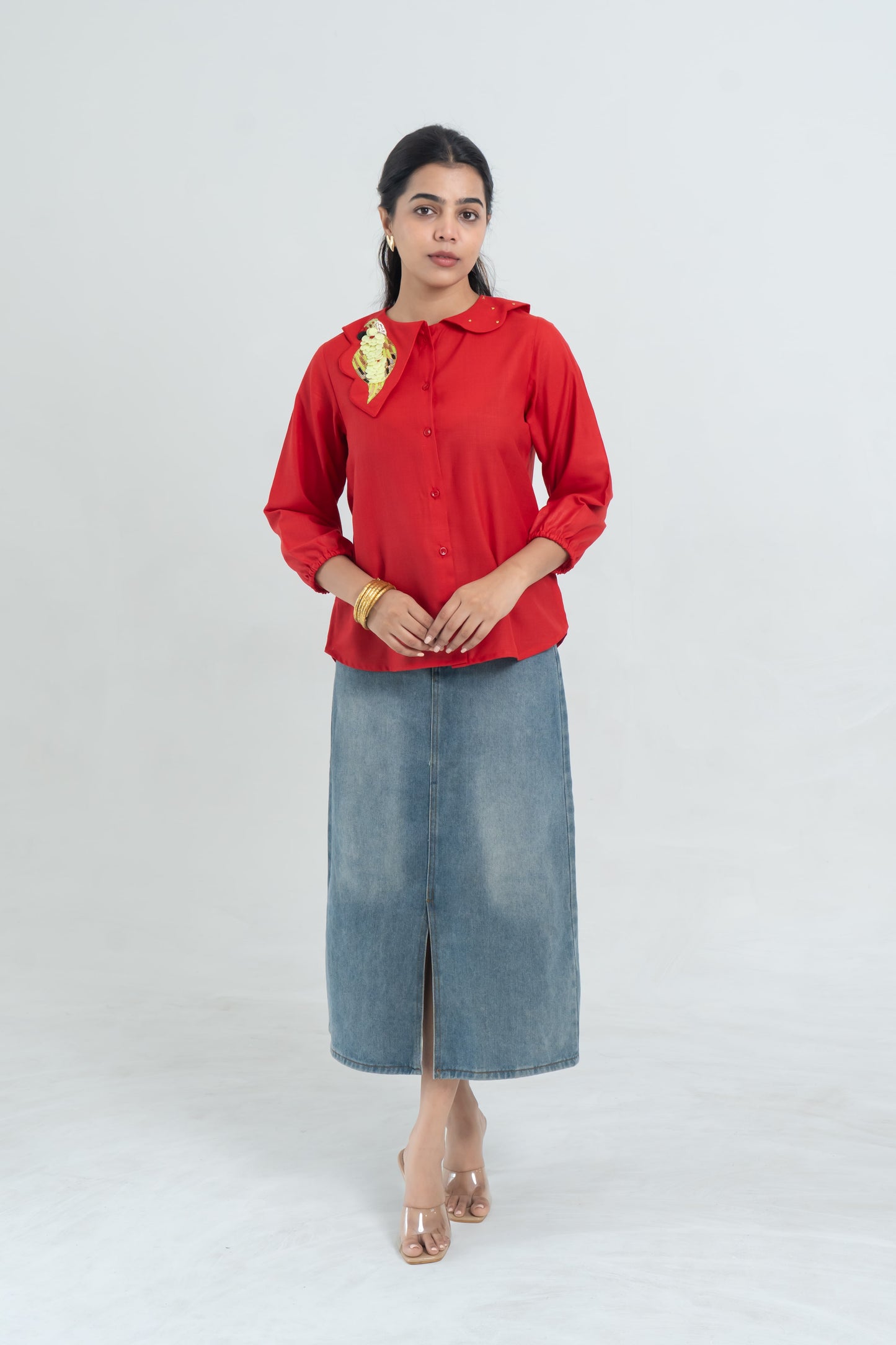 Red button-up blouse with parrot embroidery, paired with denim midi skirt and clear heels for women's fashion.