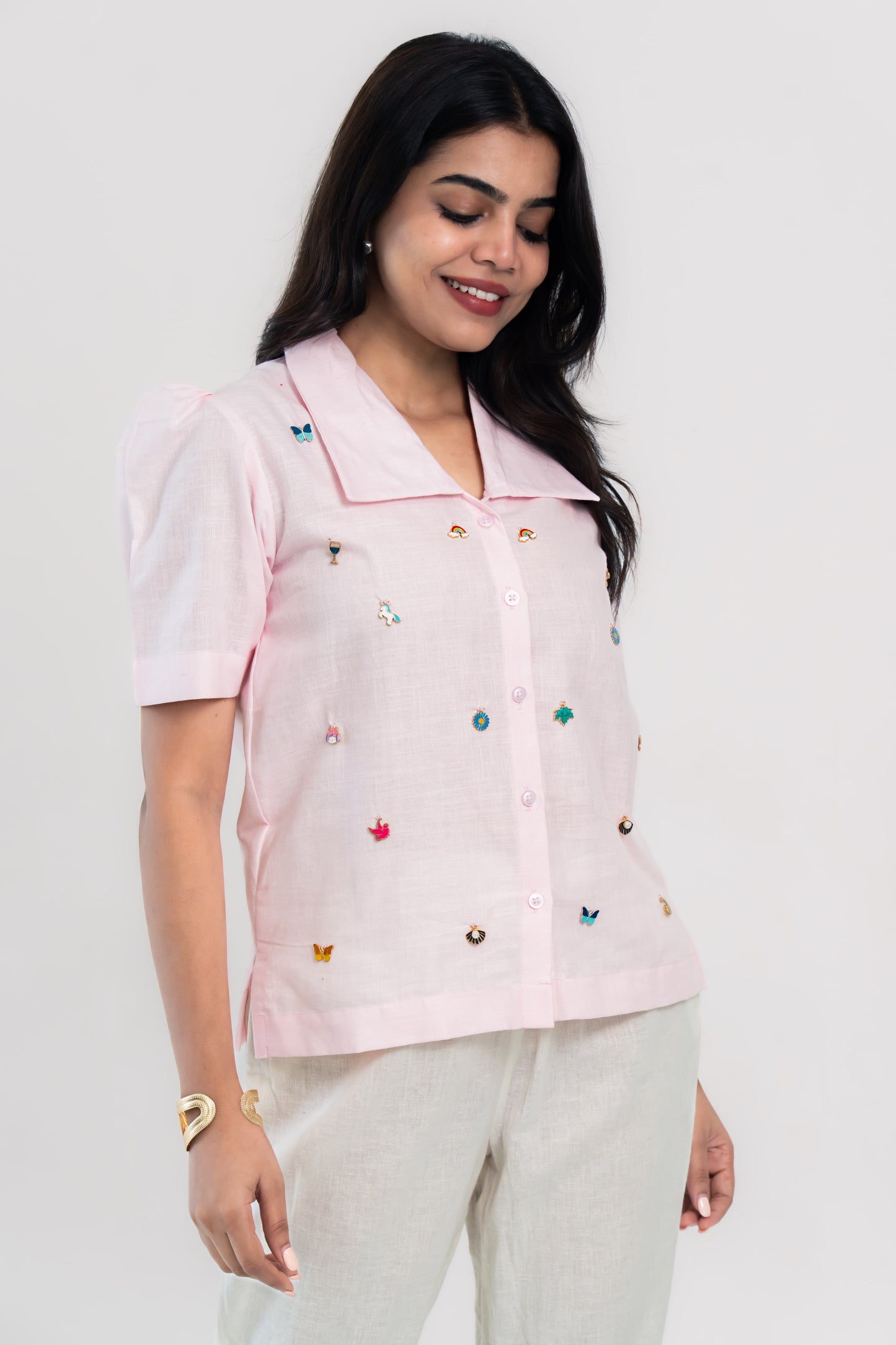 Pink embroidered blouse with colorful pins, paired with cream pants for trendy women's fashion