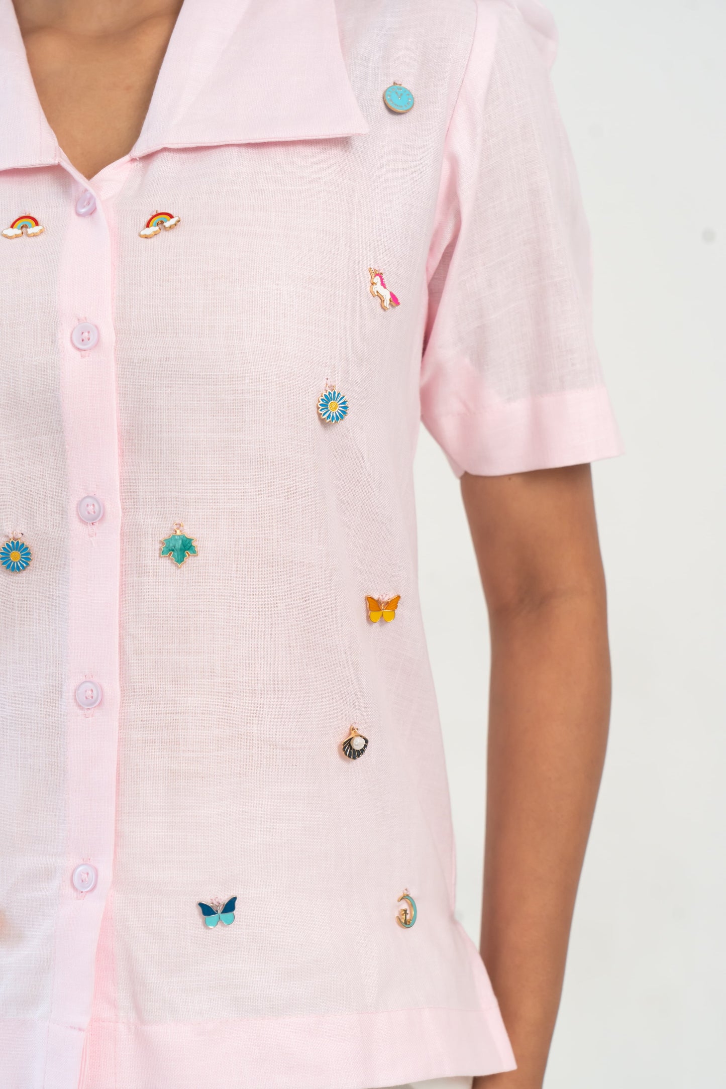 Pink button-up shirt with colorful enamel pins featuring rainbows, unicorns, butterflies, and flowers.