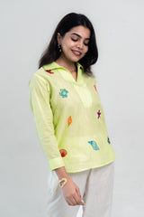 Lime green embroidered shirt with sea shell and starfish designs, paired with neutral pants for casual wear.