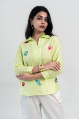 Lime green embroidered shirt with seashell designs, paired with white pants for a trendy look