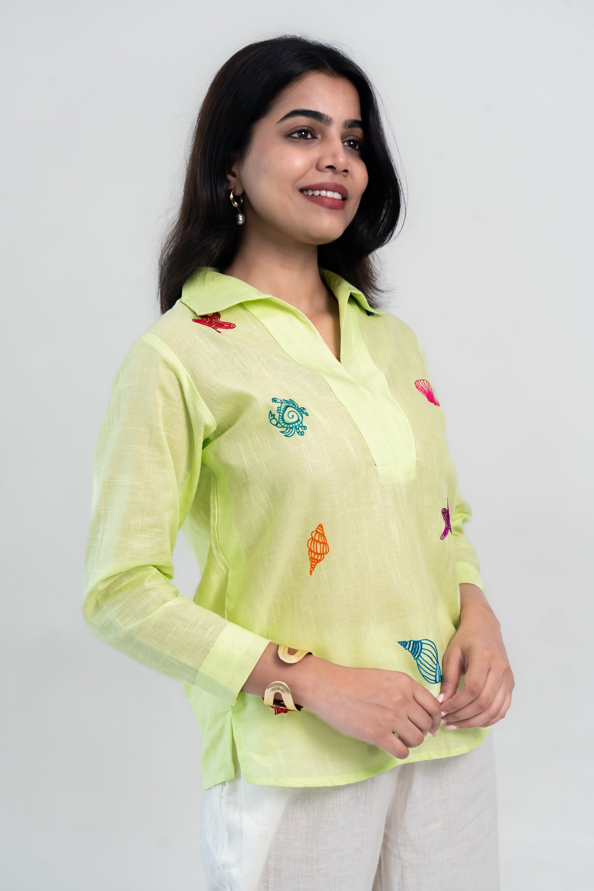 Lime green embroidered shirt with colorful shell designs, paired with white pants for a trendy look.