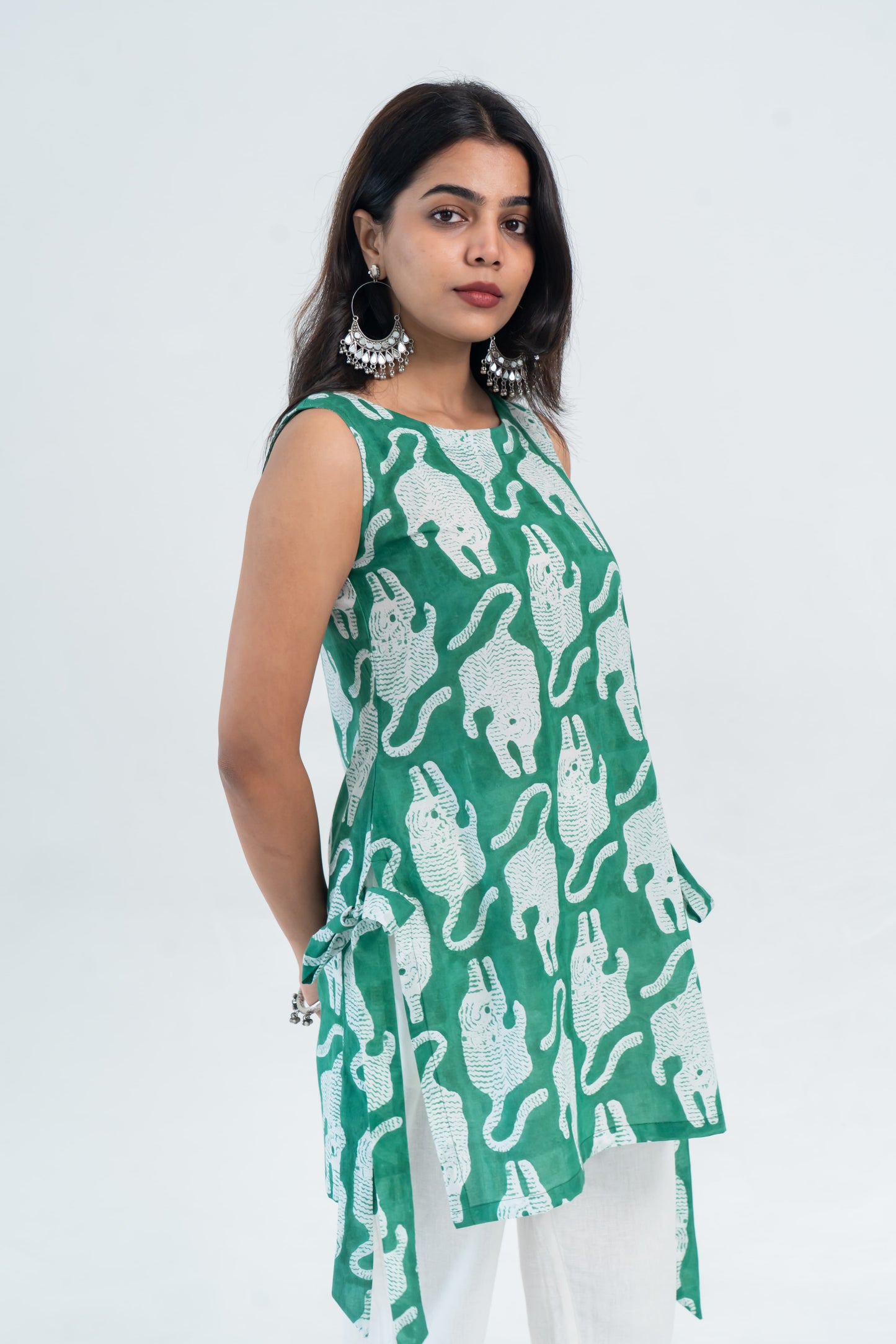 Green sleeveless top with white elephant print, side tie detail, paired with white pants for a trendy women's outfit.