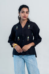 Black embroidered shirt with colorful floral details, paired with light blue jeans for a trendy casual look.