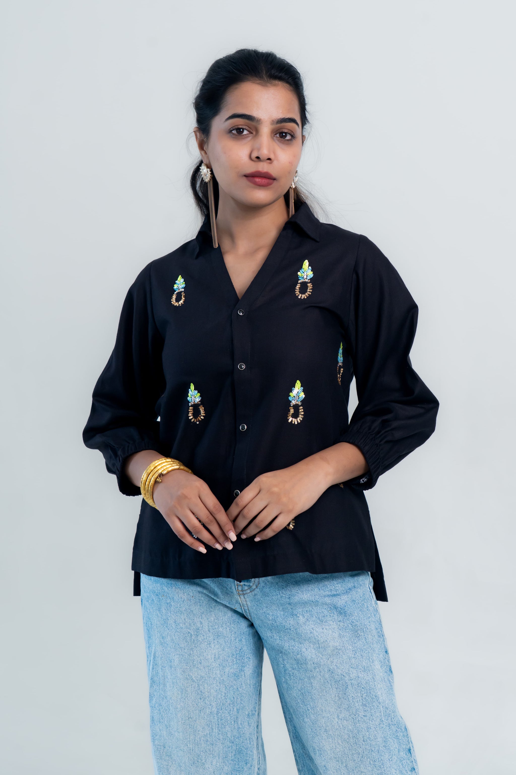 Black embroidered shirt with colorful floral details, paired with light blue jeans for a trendy casual look.