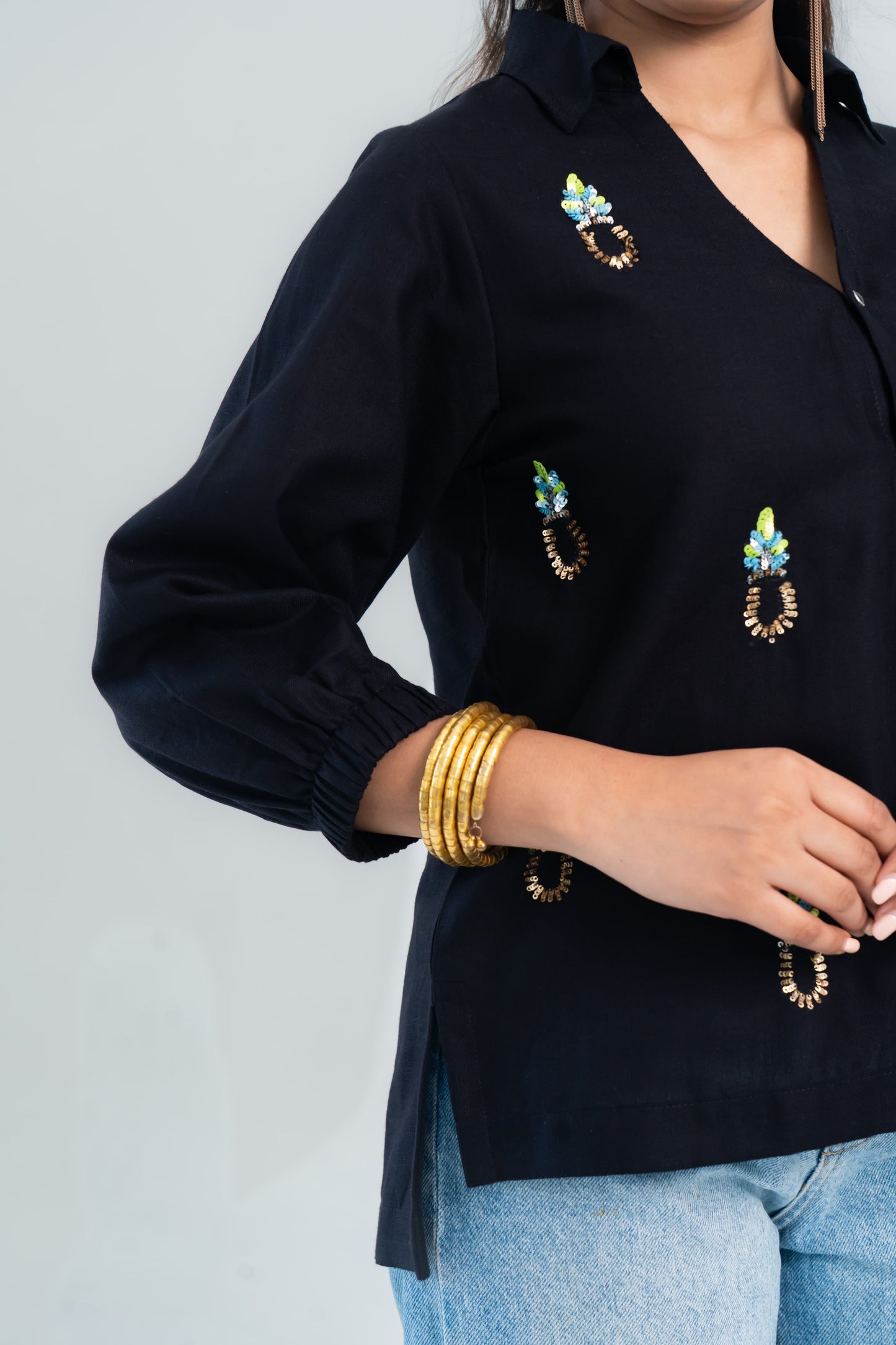 Black embroidered shirt with colorful floral details, paired with gold bangles and jeans