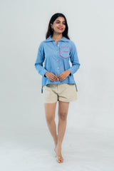 Woman in blue checkered shirt with red trim pocket and beige shorts, casual everyday style