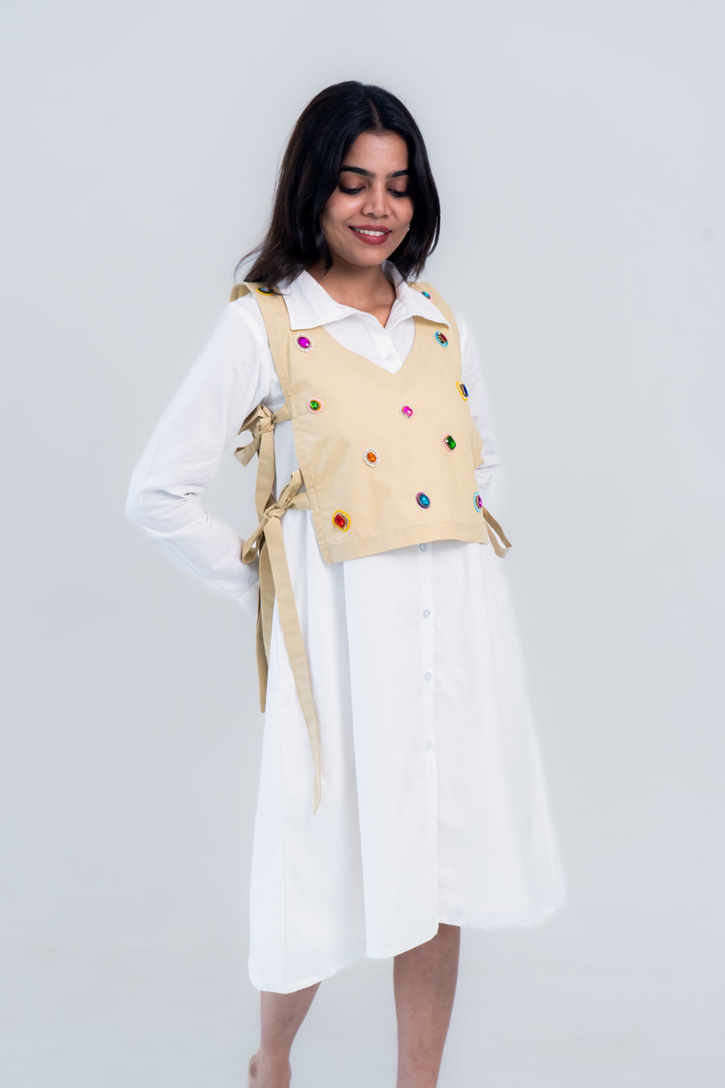 Beige vest with colorful embellishments over white shirt dress