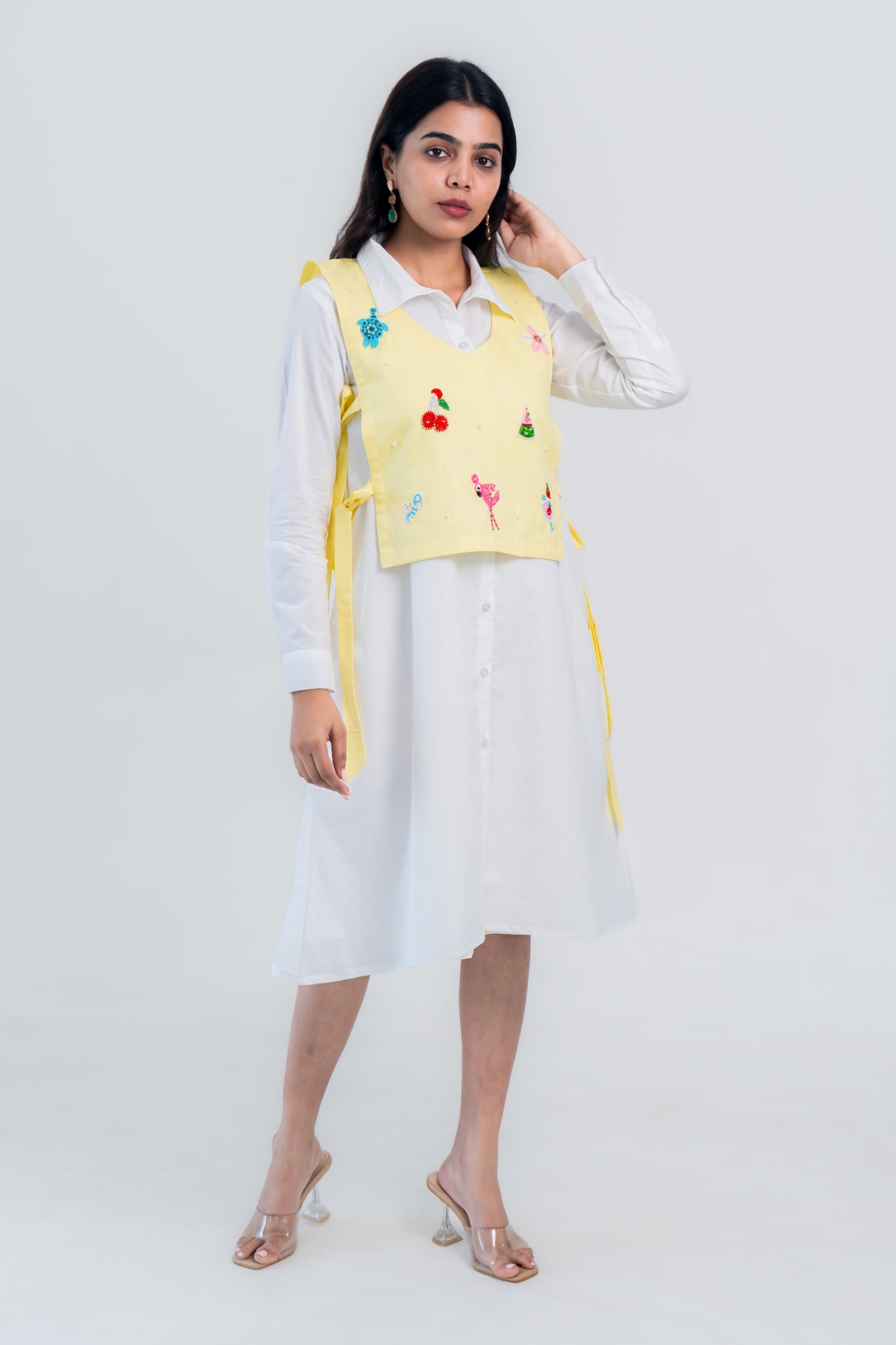 Yellow embroidered vest over white shirt dress with playful flamingo and fruit designs