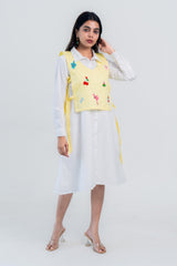 Yellow embroidered vest over white shirt dress with playful flamingo and fruit designs