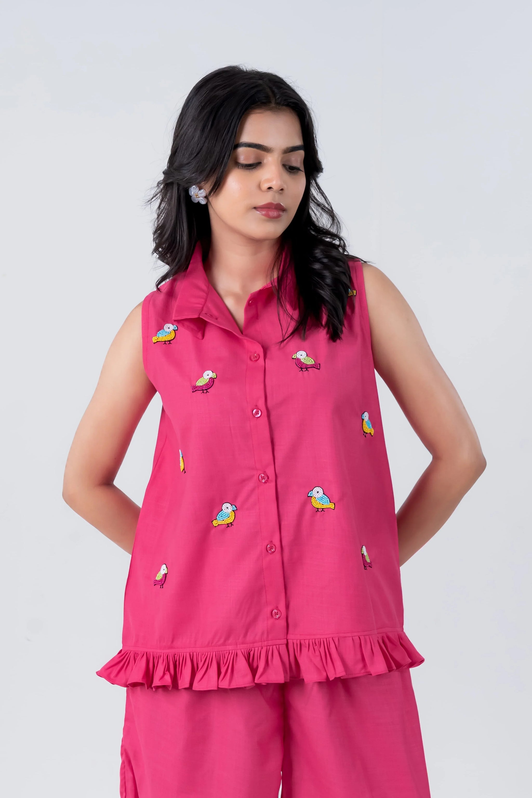 Pink sleeveless shirt with colorful bird embroidery and ruffle hem, paired with matching pants for women's casual wear