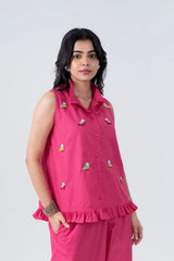 Pink sleeveless shirt with colorful bird embroidery and ruffled hem, paired with matching pants