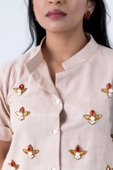 Beige button-up top with red gem and pearl bee embroidery, styled with matching earrings.