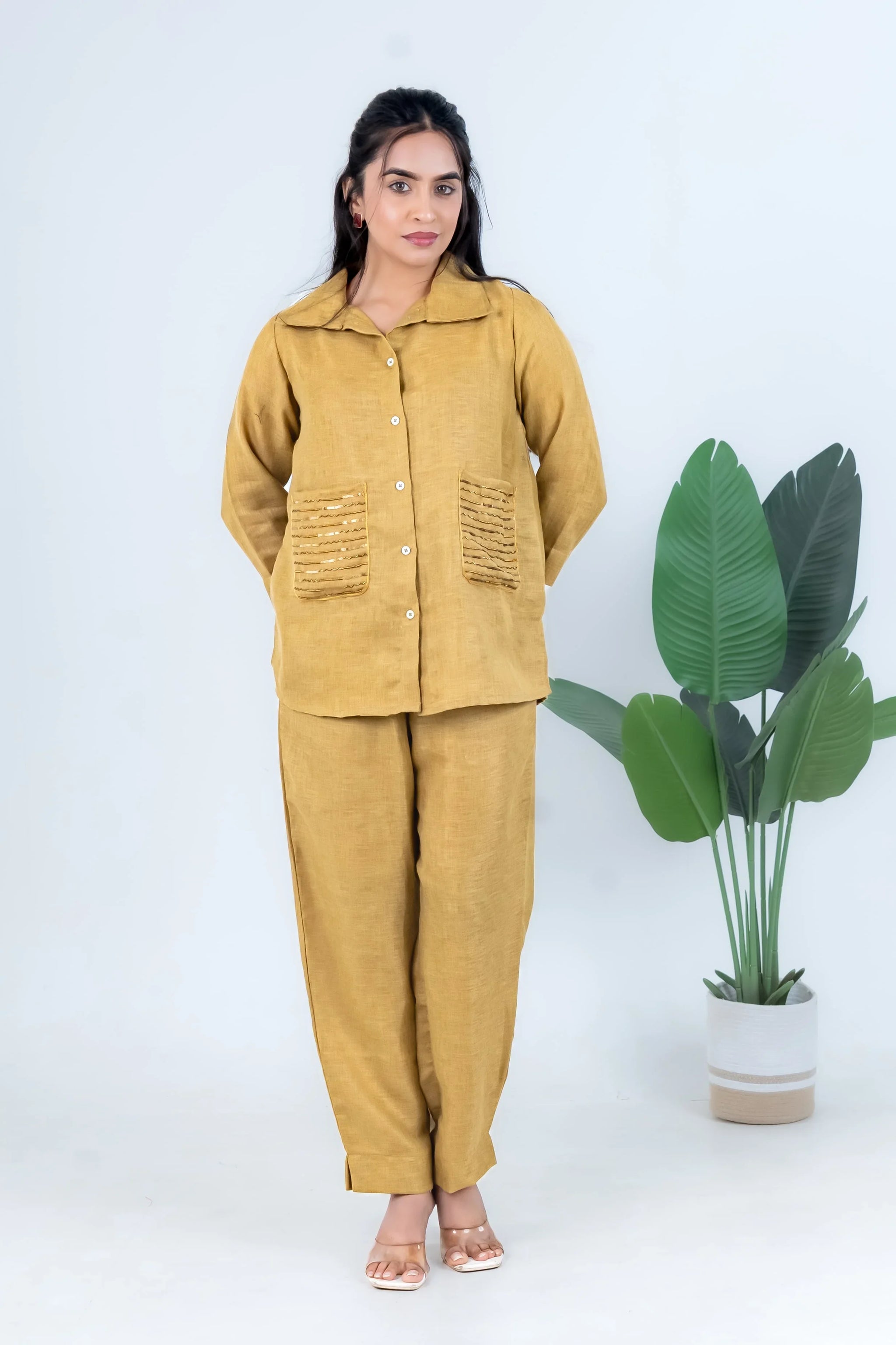 Mustard yellow linen co-ord set with button-up top and wide-leg pants, styled with sandals and green plant