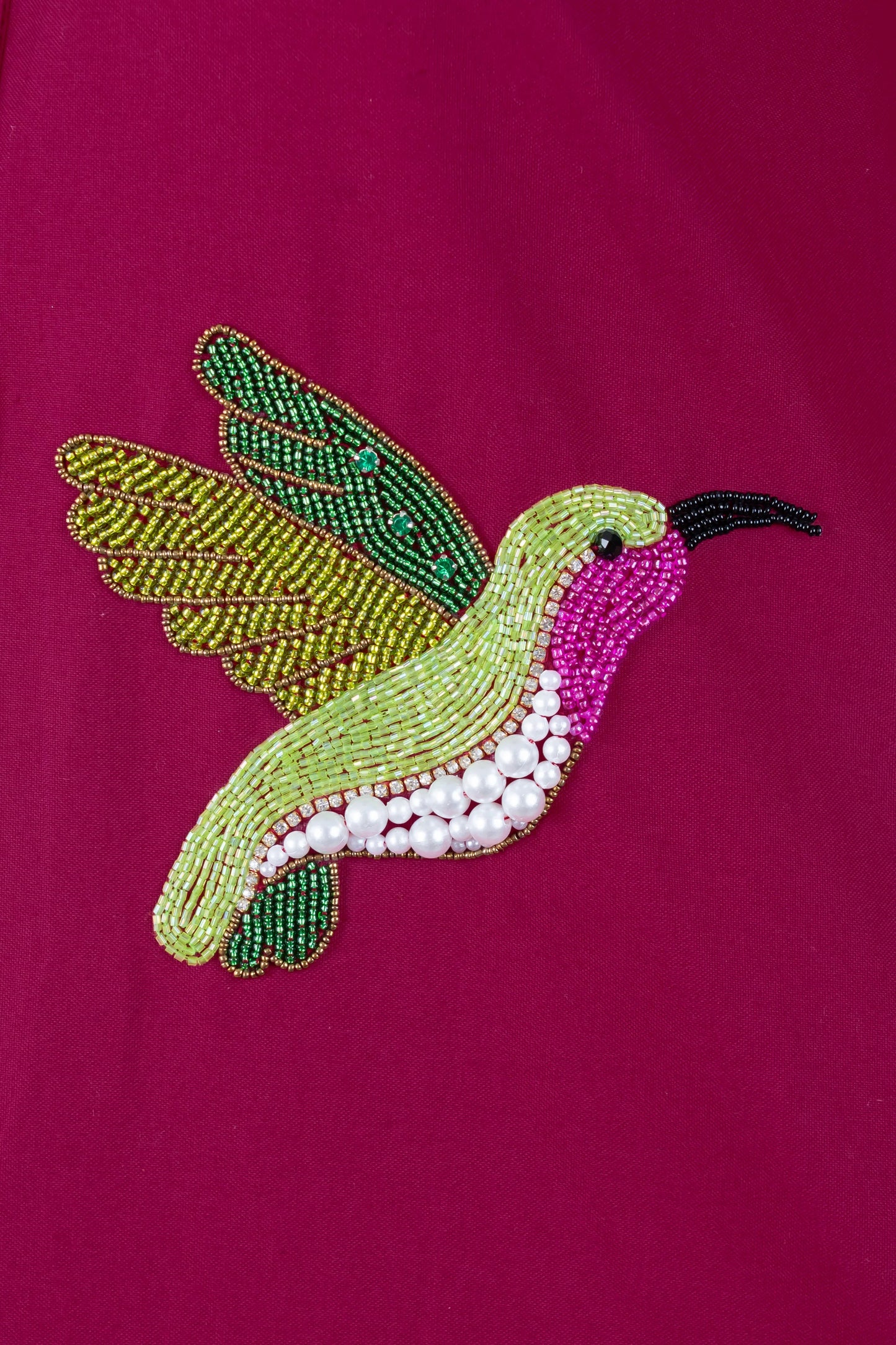 Beaded hummingbird embroidery with green, pink, and pearl details on magenta fabric