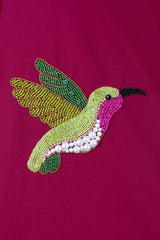 Beaded hummingbird embroidery with green, pink, and pearl details on magenta fabric