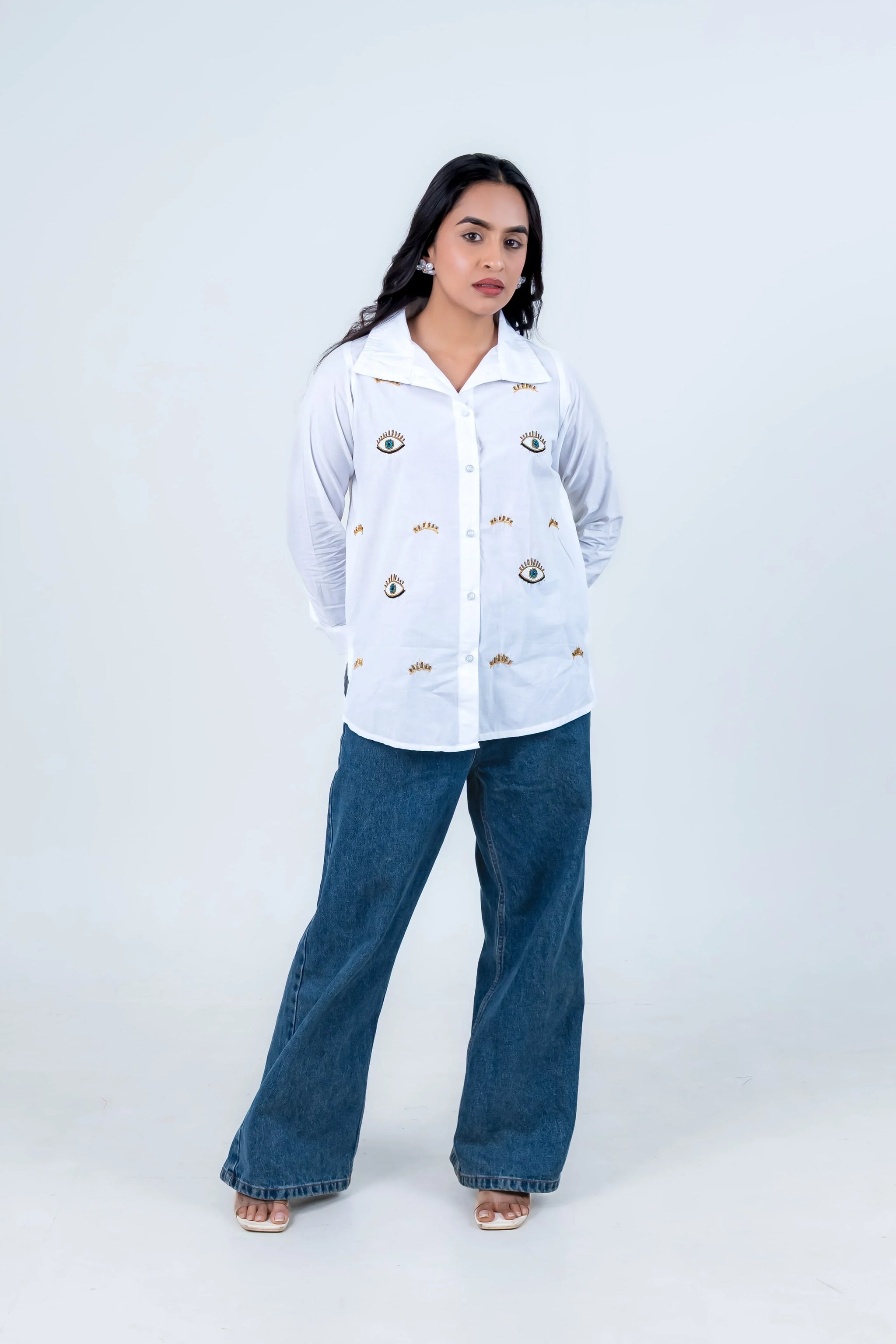 Woman in white embroidered shirt with eye motifs and wide-leg jeans, stylish casual outfit