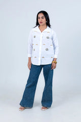 White button-down shirt with eye embroidery, paired with blue wide-leg jeans and sandals.